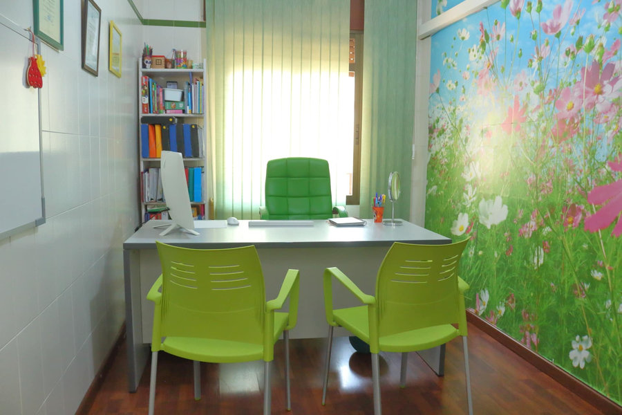 Despacho de logopedia, con mesa de trabajo, estantería con material didáctico y mural infantil de flores