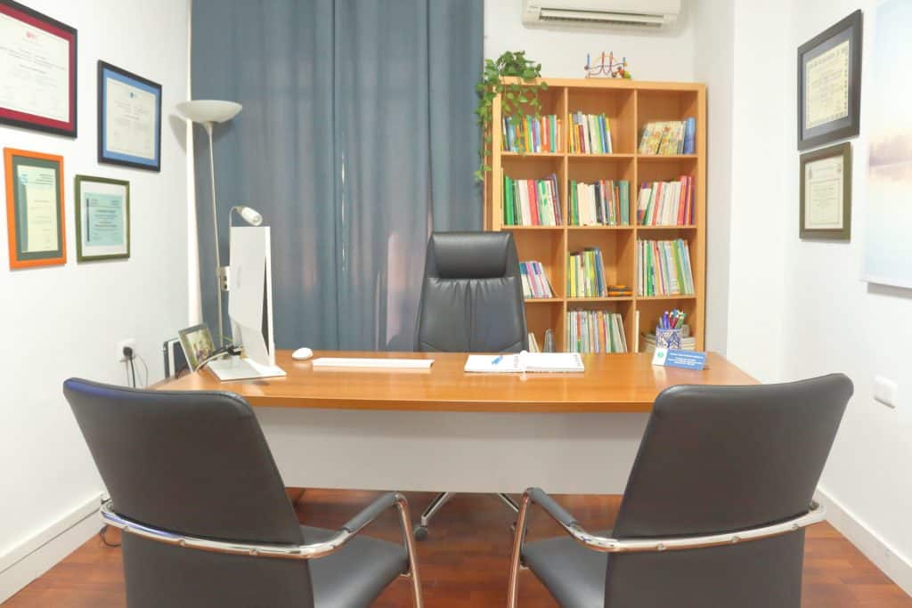 Despacho de psicología de Carmen Irene Jiménez Bujalance, con mesa de trabajo, estantería y diplomas en la pared